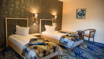 A hotel room with two beds, a small table, a chair, and a painting on the wall.
