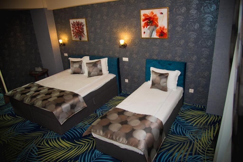 A hotel room with two beds, each with a headboard, a small bedside table, and a wall-mounted light.
