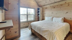 A bedroom with a wooden ceiling, a bed with striped bedding, a window, and a desk with a remote control. - Breathless Views by Smoky Cove Resort (Sevierville)