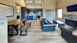 A spacious living area with a wooden ceiling, a dining table with benches, a sofa, a fireplace, and a kitchen in the background. - Breathless Views by Smoky Cove Resort (Sevierville)
