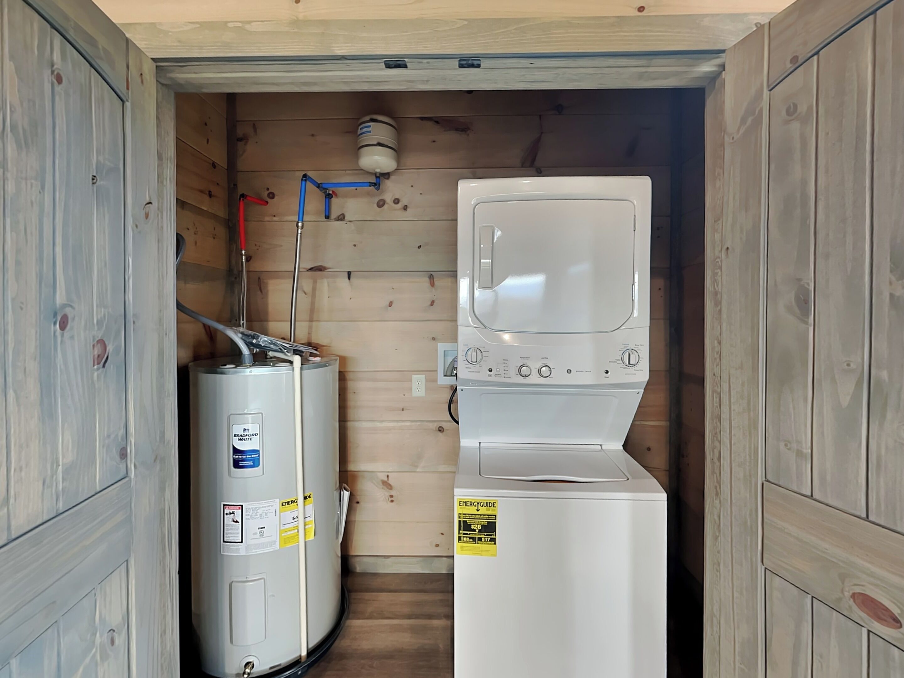 A compact laundry room with a white washer and dryer, a water heater, and a visible plumbing system.