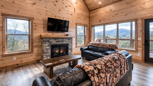 A cozy cabin interior with a stone fireplace, leather seating, and large windows offering mountain views. - Breathless Views by Smoky Cove Resort (Sevierville)