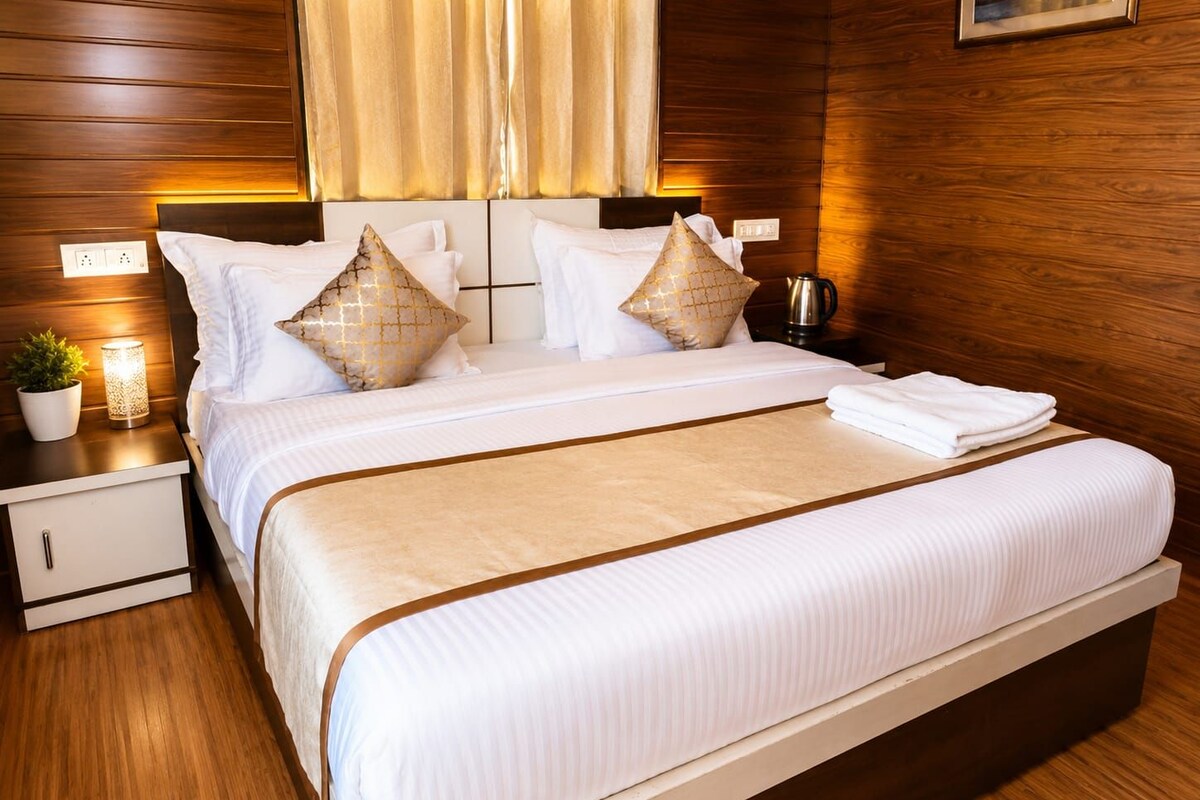 A hotel room with a large bed, wooden paneling, a nightstand with a lamp, and a painting on the wall.