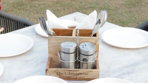 A dining table with three white dishes containing food, a wooden salt and pepper shaker set, and a white plate. - The Udaisarovar - Lakeside Paradise (Udaipur)