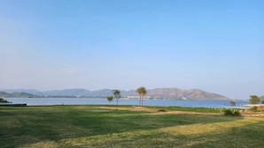 A grassy field with a body of water and mountains in the background. - The Udaisarovar - Lakeside Paradise (Udaipur)
