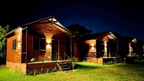 A row of wooden cabins with exterior lighting, a grassy lawn, and a dark sky. - The Udaisarovar - Lakeside Paradise (Udaipur)