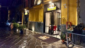 A restaurant with a glass door entrance, outdoor seating, and a visible number '26' on the wall. - Window in the Stone Naples (Naples)