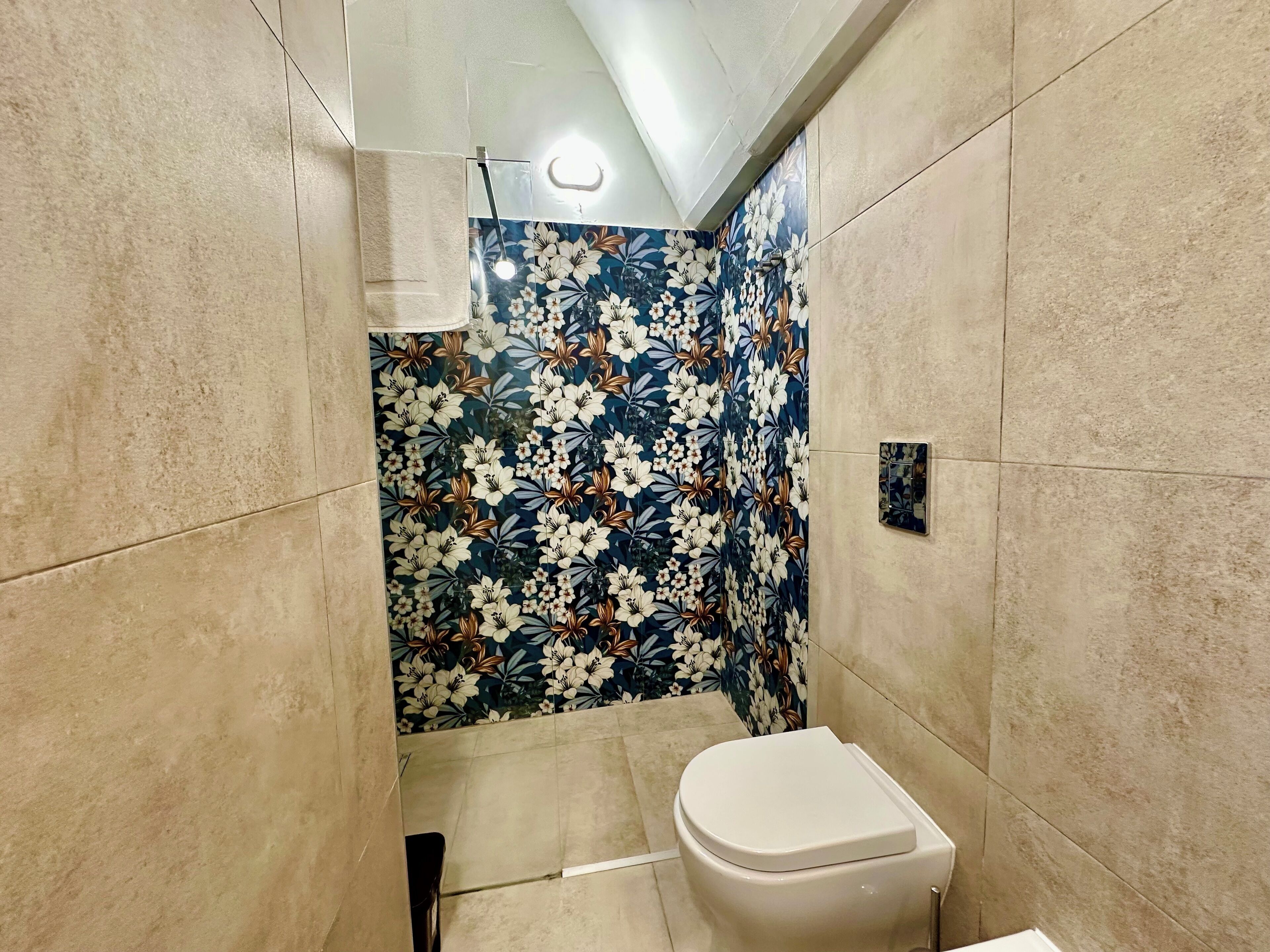A bathroom with a toilet, a shower area with floral-patterned tiles, and a light fixture on the ceiling.