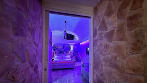 A room with a stone wall, a bed with pillows, a ceiling fan, and a mounted projector. - Window in the Stone Naples (Naples)
