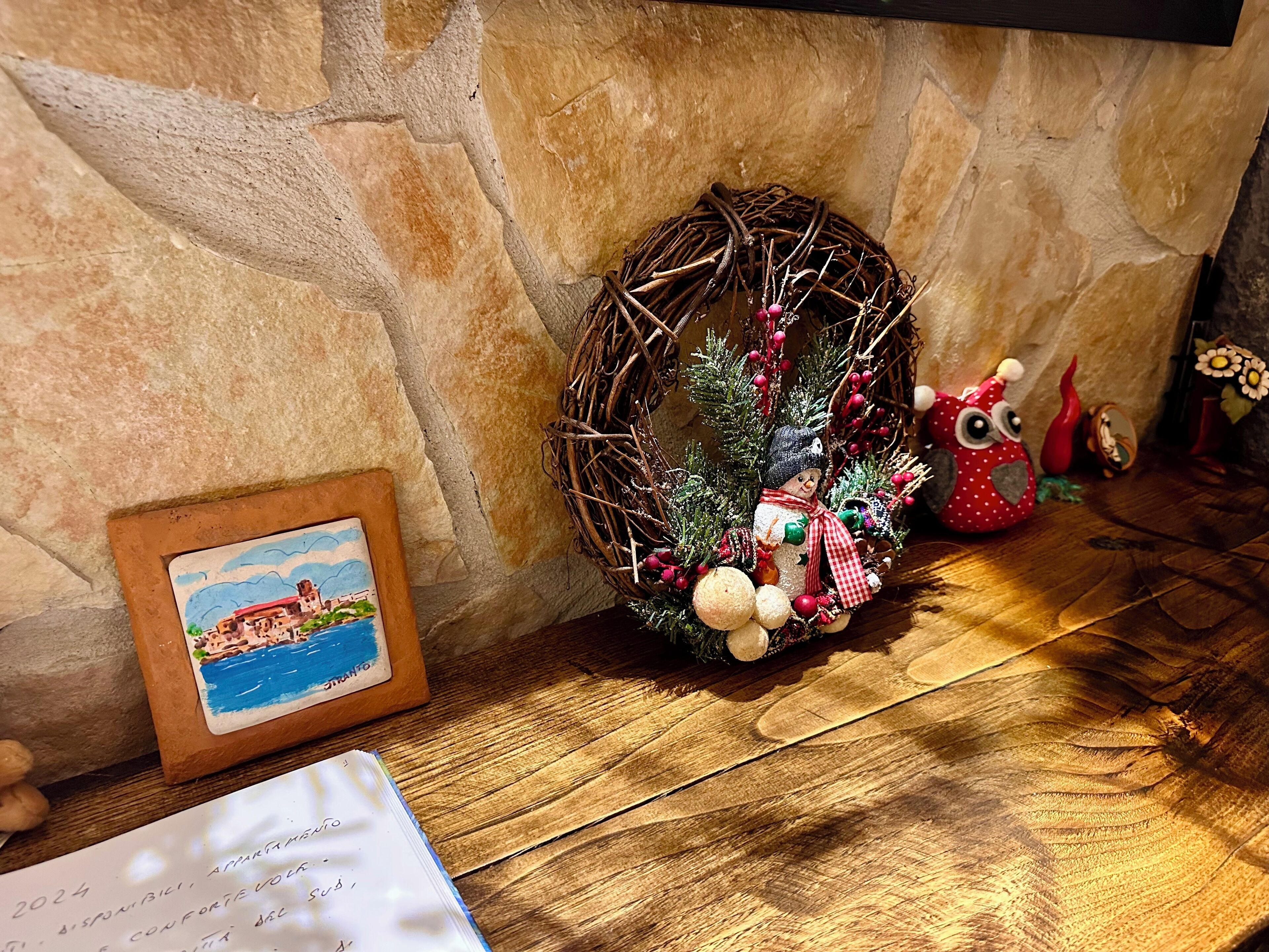 A rustic stone wall, a small wreath with decorations, a framed picture, and a notebook on a wooden surface.