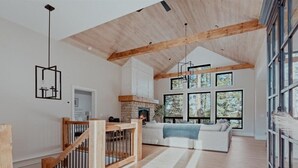 Un amplio salón con techo alto, vigas de madera, chimenea y ventanas grandes que ofrecen vistas al exterior.