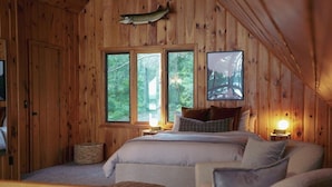 Um quarto de cabana aconchegante com uma cama grande, paredes de madeira e um peixe montado na parede.