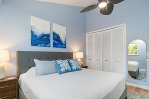 Een slaapkamer met een bed, twee wanddecoraties, een plafondventilator, een bedlamp, een nachtkastje en een kledingkast.