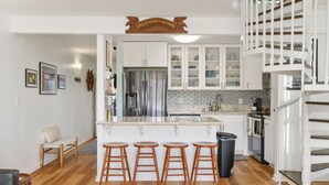 A modern kitchen with a central island, bar stools, and a sign above the island. - Pu'uhonua Kai ~ Oceanside Refuge (Kahuku)