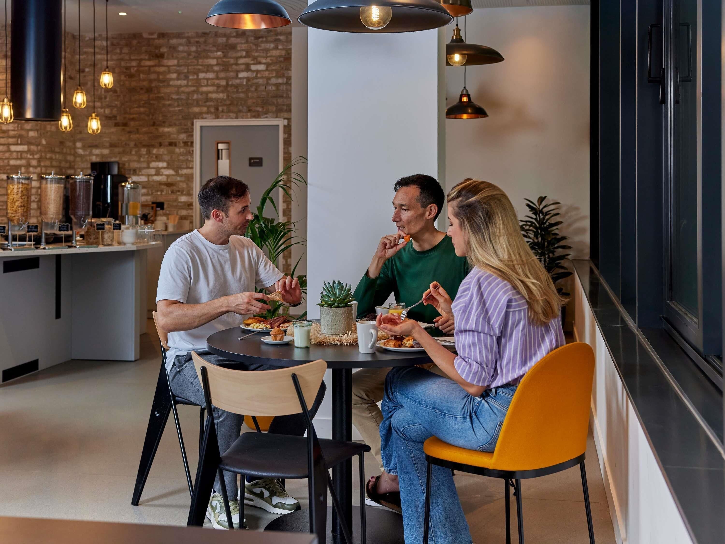 Un espace repas moderne avec un mur en briques, des luminaires suspendus et une cuisine en arrière-plan.