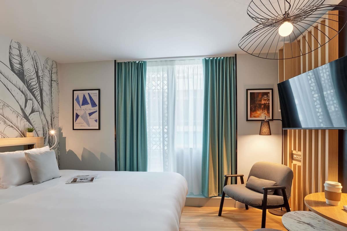 Et hotelværelse med en seng, en stol, et bord og et fjernsyn.