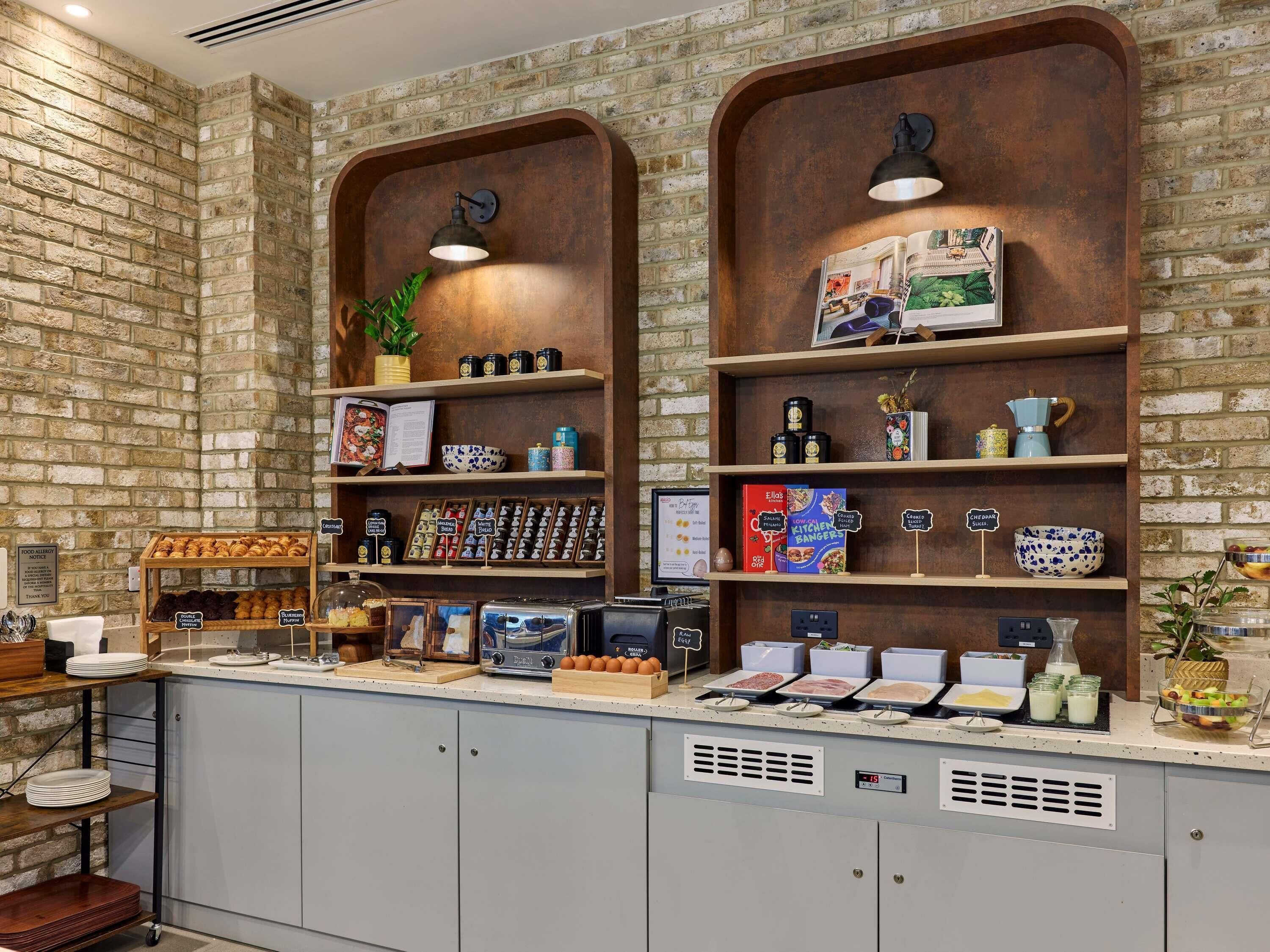 Un bar pour le petit-déjeuner avec un mur en briques en arrière-plan, des étagères remplies de produits alimentaires et une machine à café.