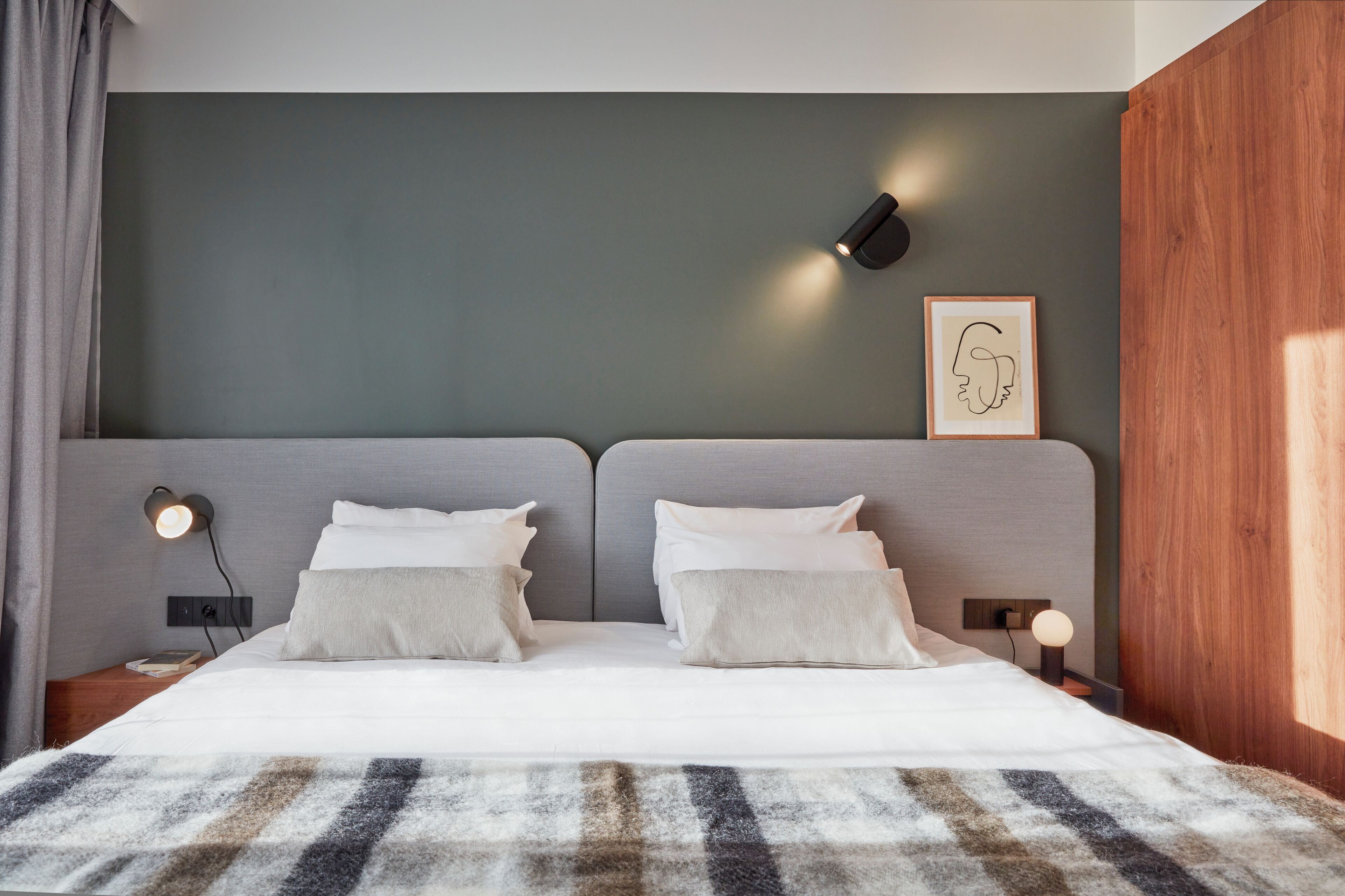 Quarto moderno com uma cama grande, duas mesas de cabeceira, uma luminária na parede e uma obra de arte emoldurada.
