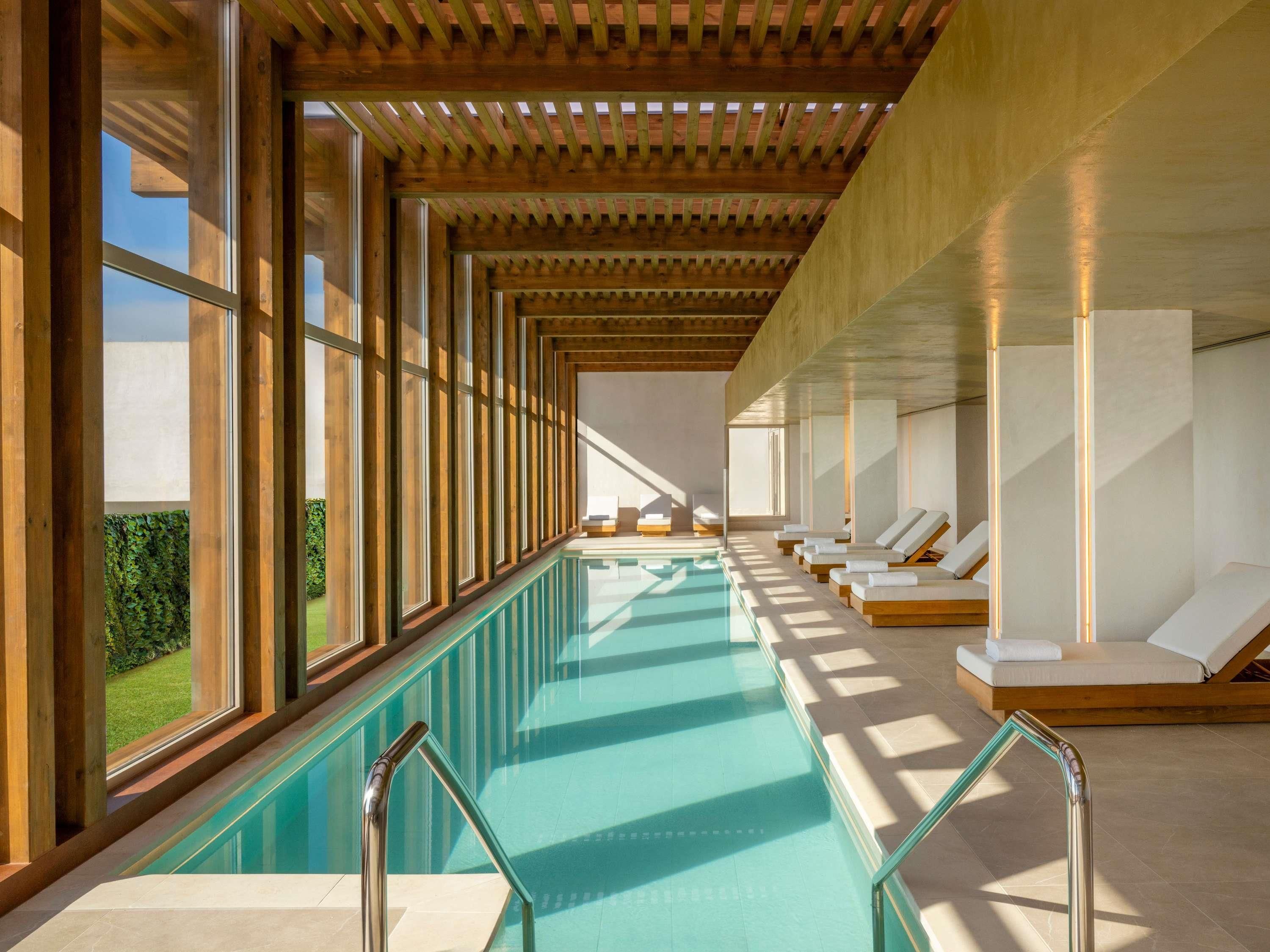 A swimming pool with sunlit loungers and a view of greenery outside.