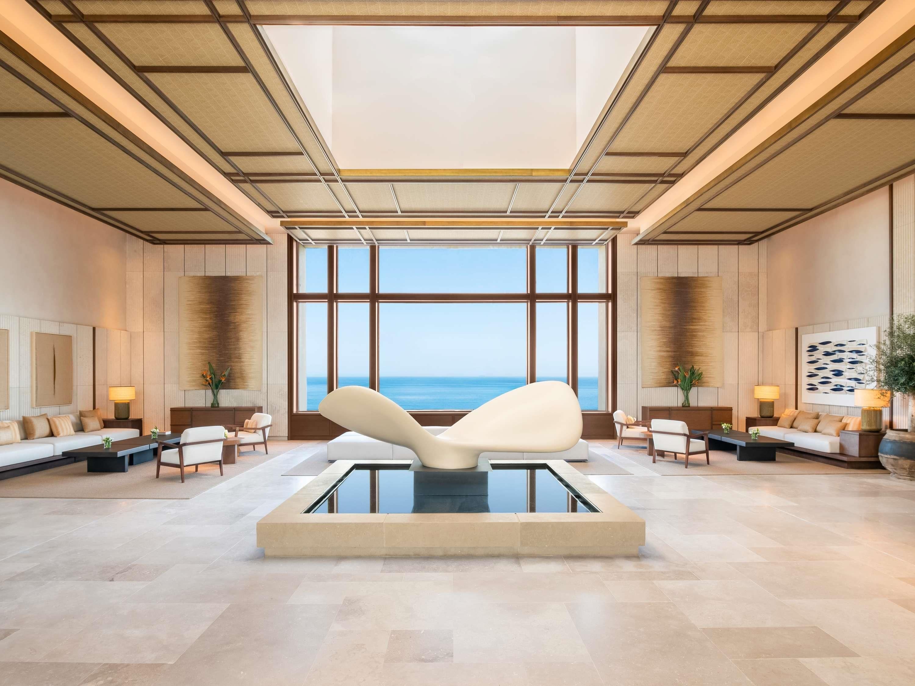 Eine großzügige Lobby mit einem großen Fenster mit Meerblick, einer zentralen Sitzecke und einem modernen Design mit Holzvertäfelung und hoher Decke.