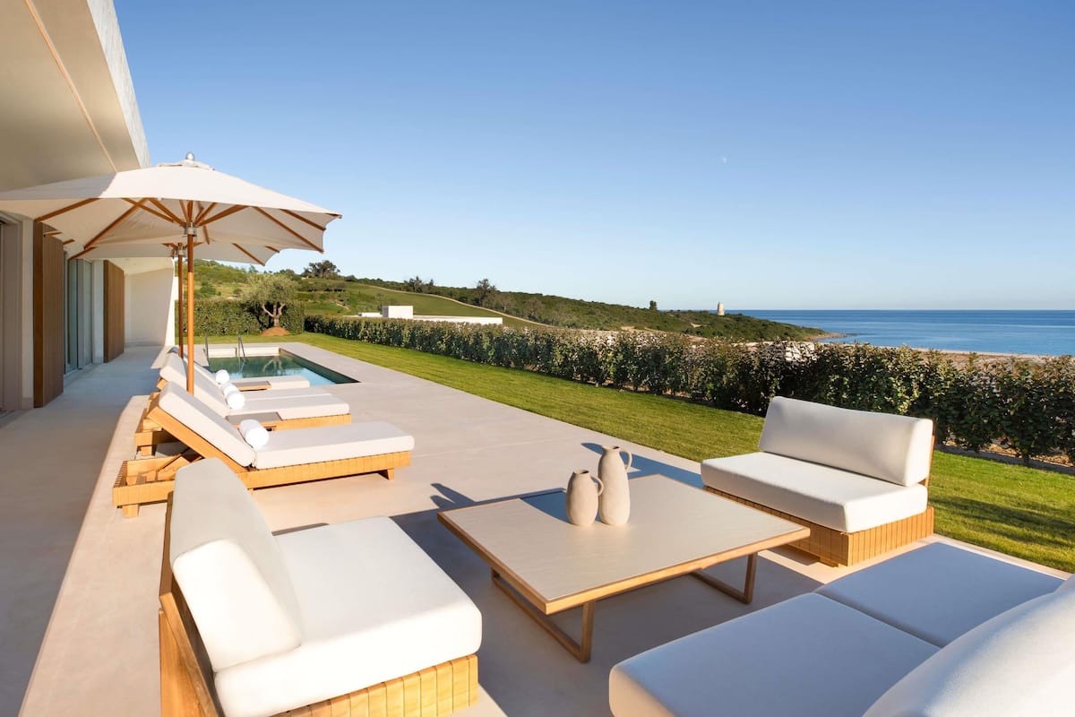 Un área junto a la piscina con sillones, una mesa y vista al mar.