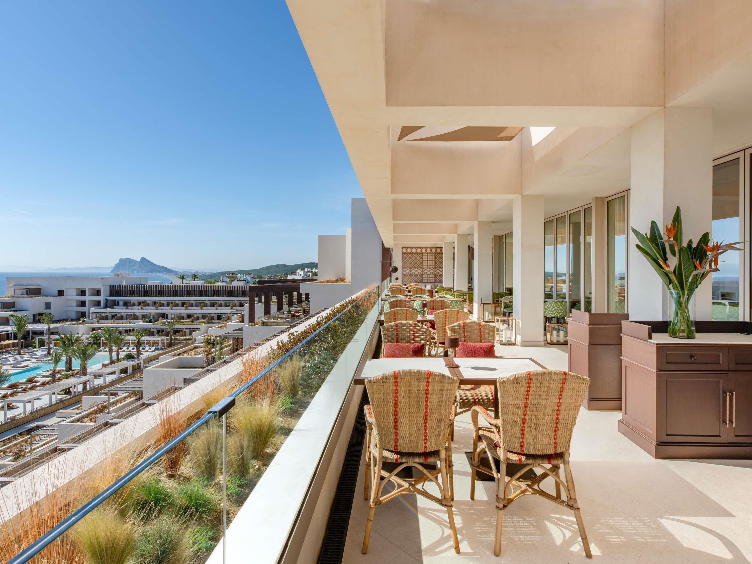 A balcony with outdoor seating, a pool, and a view of the sea and buildings.
