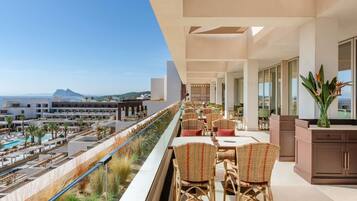 A balcony with outdoor seating, a pool, and a view of the sea and buildings.