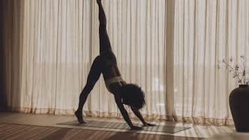 A person performing a yoga pose on a mat in a room with sheer curtains and a potted plant.
