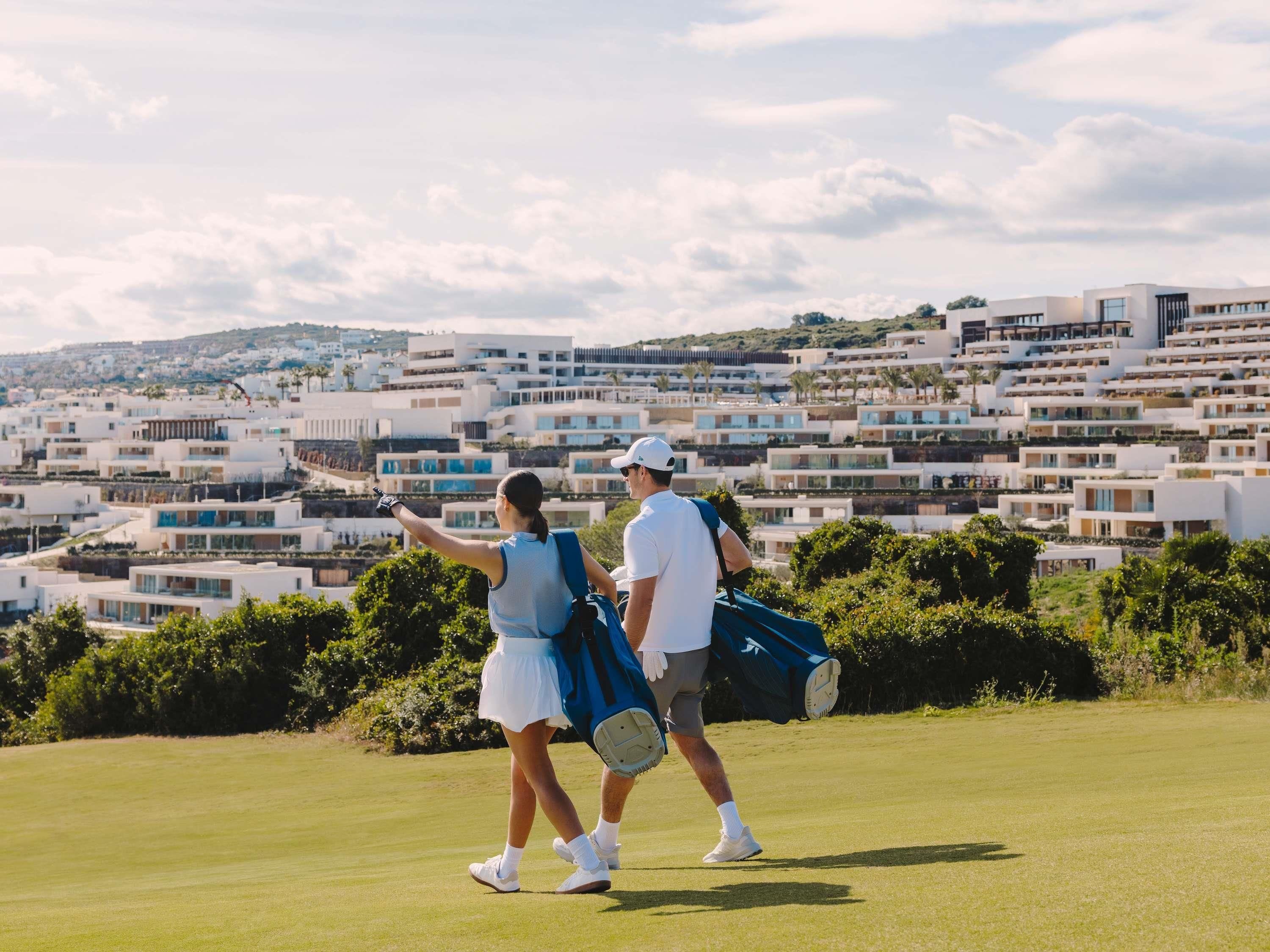 A couple on a golf course with modern buildings in the background.