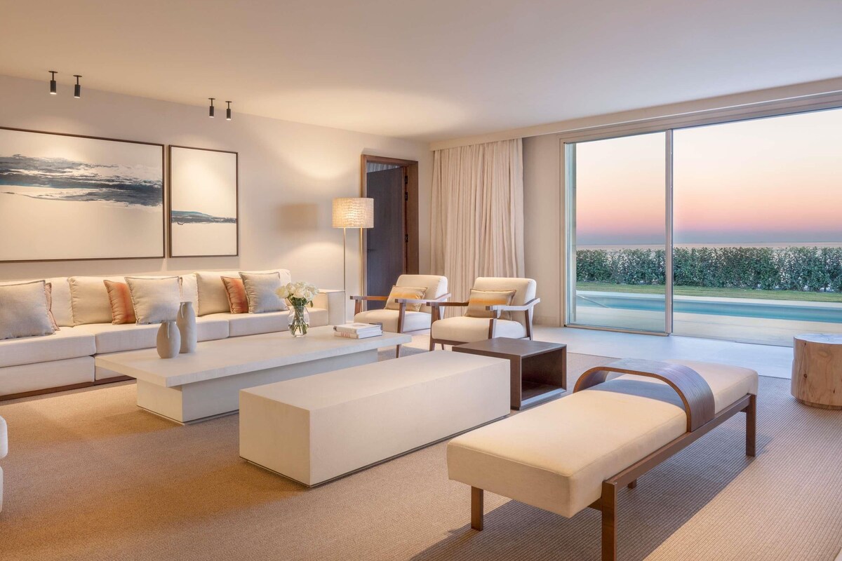 Un salon moderne avec un canapé, des fauteuils, un banc et une grande fenêtre donnant sur un beau paysage.