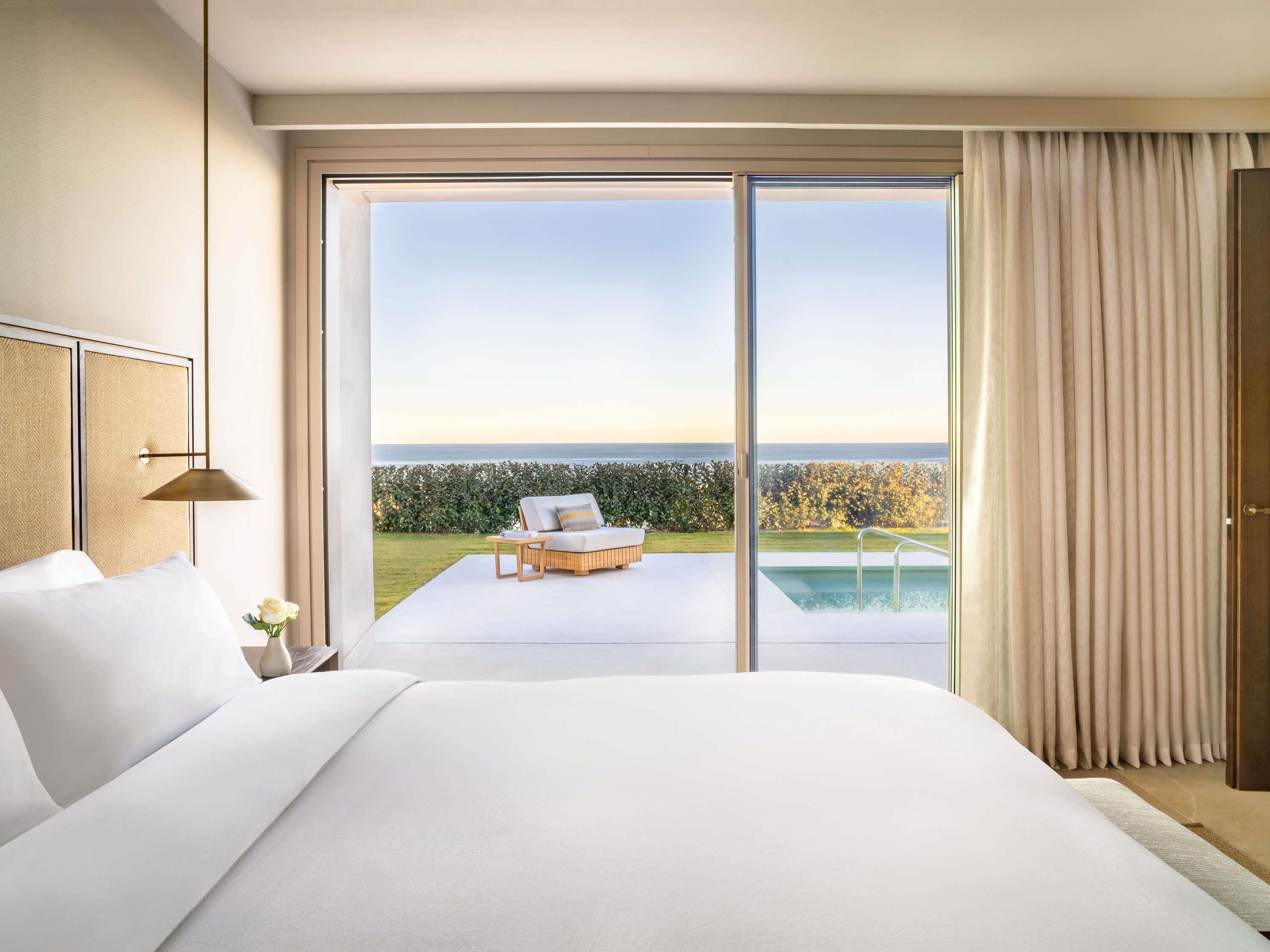 A bedroom with a large bed, a view of the sea, and a pool outside.