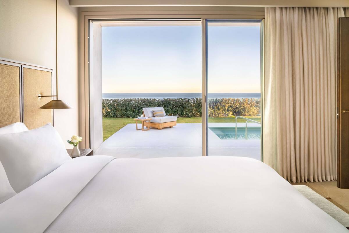 Une chambre avec un grand lit, une vue sur la mer et une piscine à l’extérieur.