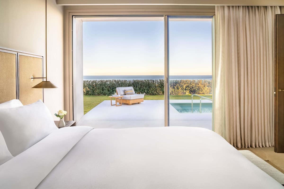 A bedroom with a large bed, a view of the sea, and a pool outside.