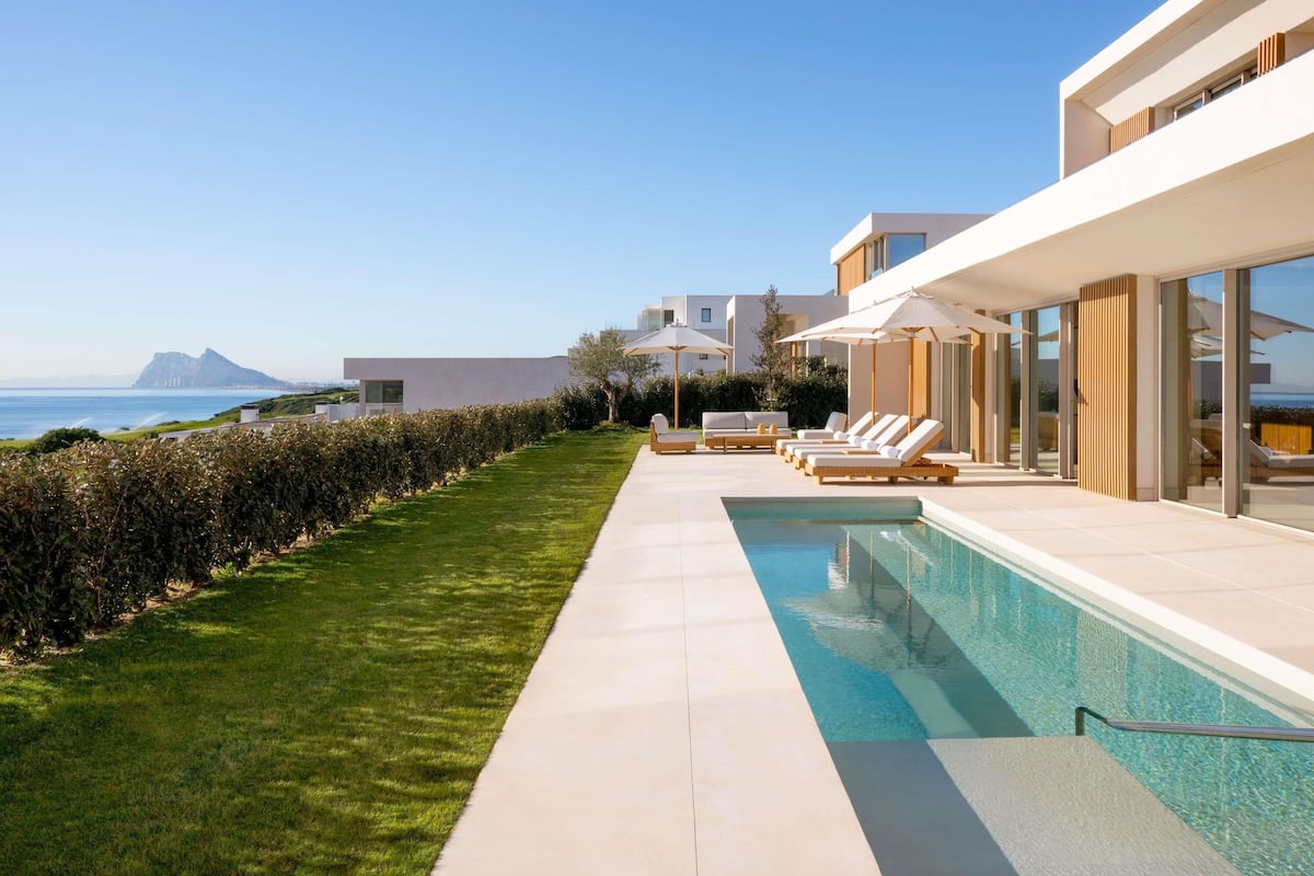 A modern poolside area with lounge chairs, a swimming pool, and a view of the sea.