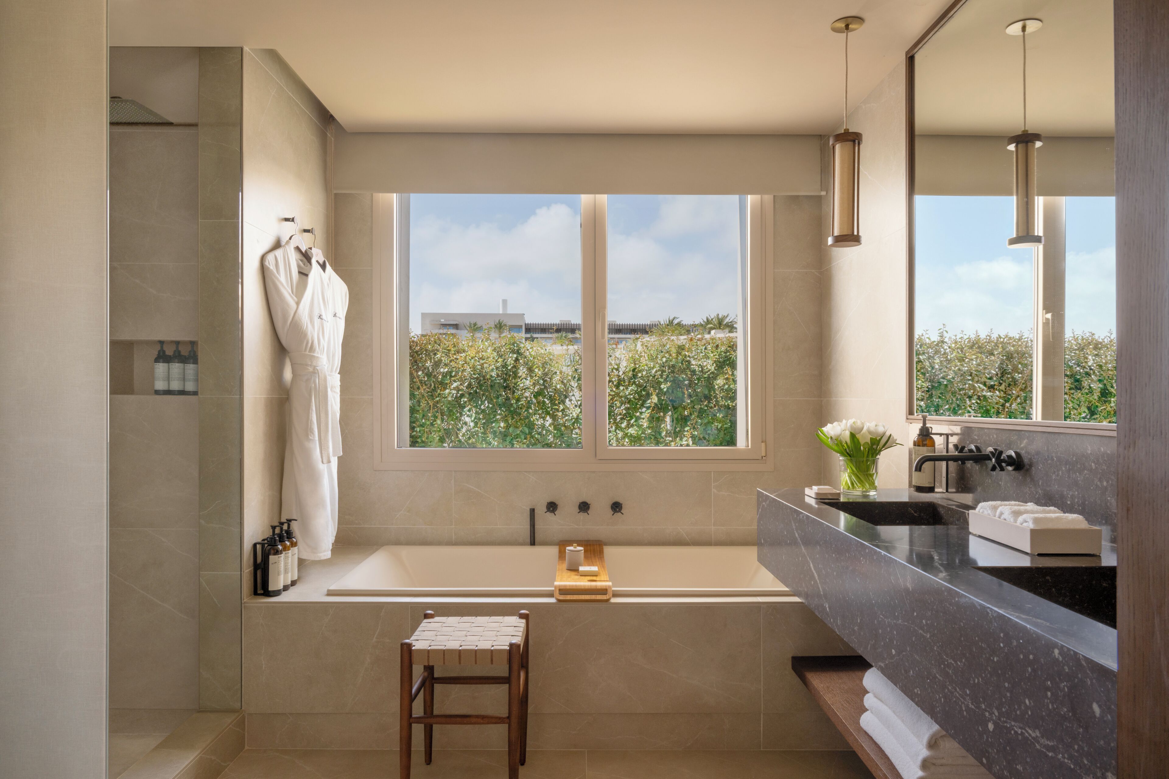 Un baño moderno con una bañera grande, un tocador con lavabo, un espejo y una ventana que ofrece vistas al exterior.