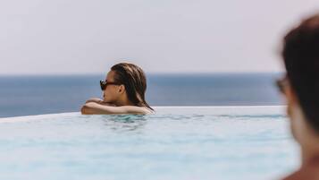 En person som kopplar av i en vacker, turkosblå pool som ser ut att sträcka sig oändligt långt, med utsikt över havet.