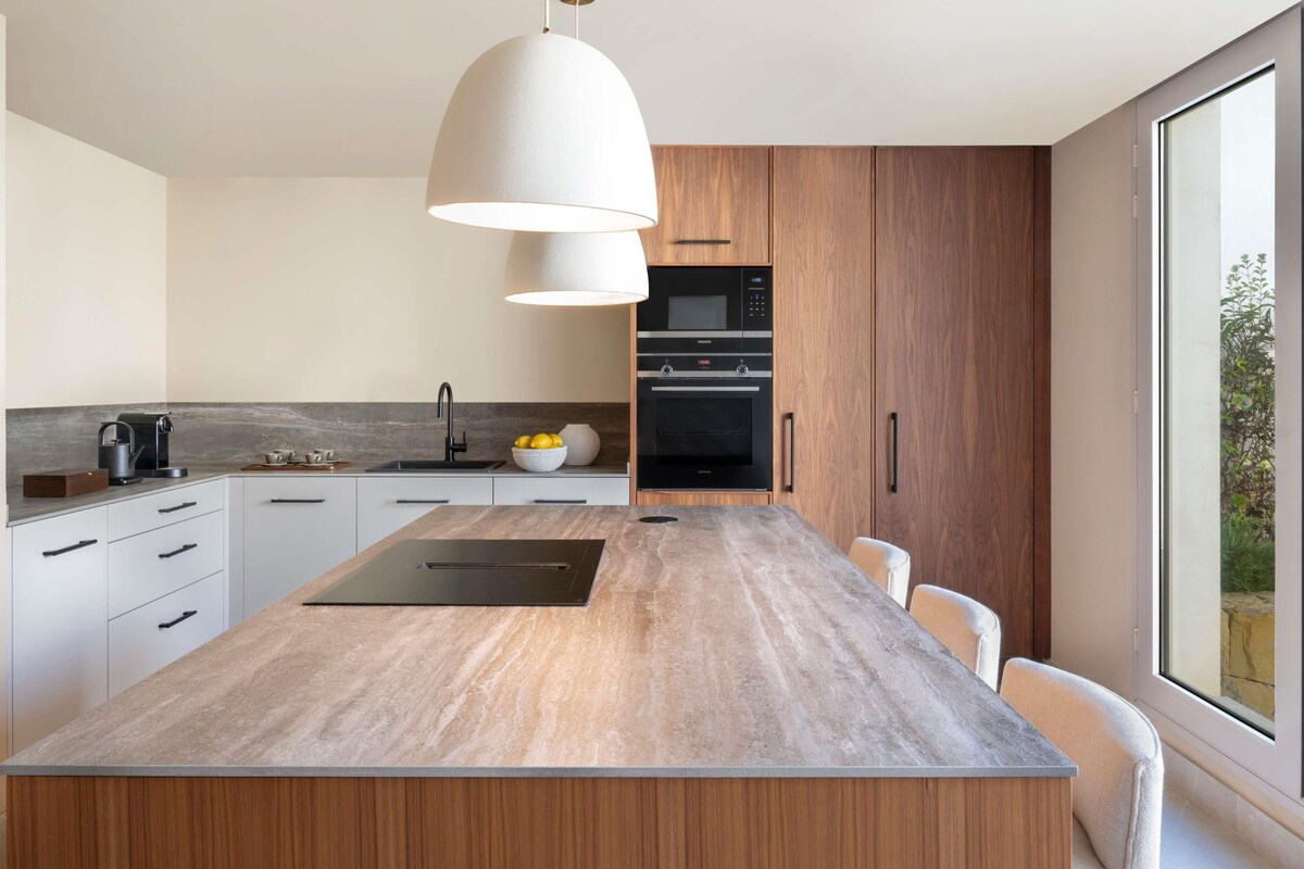 Une cuisine moderne dotée d’un îlot central, d’appareils électroménagers intégrés et d’une grande fenêtre.