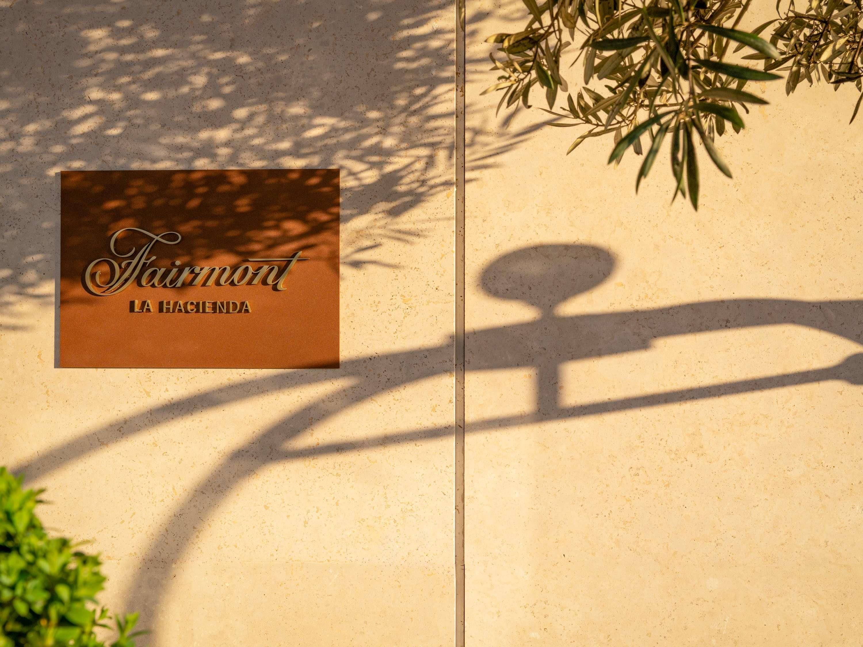 Um letreiro com o texto 'Fairmont LA HAGUENDA' em uma parede bege.
