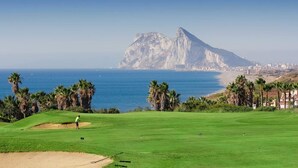 Un parcours de golf offrant une vue sur une ville côtière et sur une montagne imposante en arrière-plan.