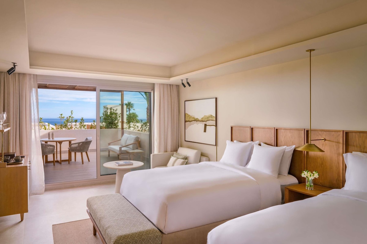 Une chambre d’hôtel avec deux lits, un balcon avec une table et des chaises, et une vue sur l’océan.