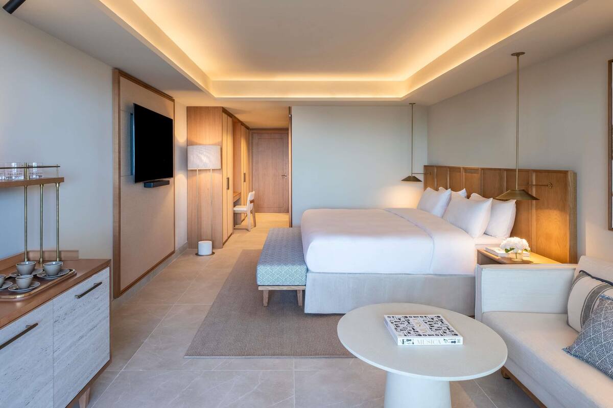 Habitación de hotel moderna con una cama grande, una mesita de noche, un sofá, una pequeña mesa redonda, un televisor montado en la pared y un armario de madera.