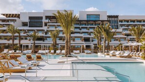 Ein modernes Hotel mit großzügiger Poolanlage, zahlreichen Liegestühlen und Palmen.