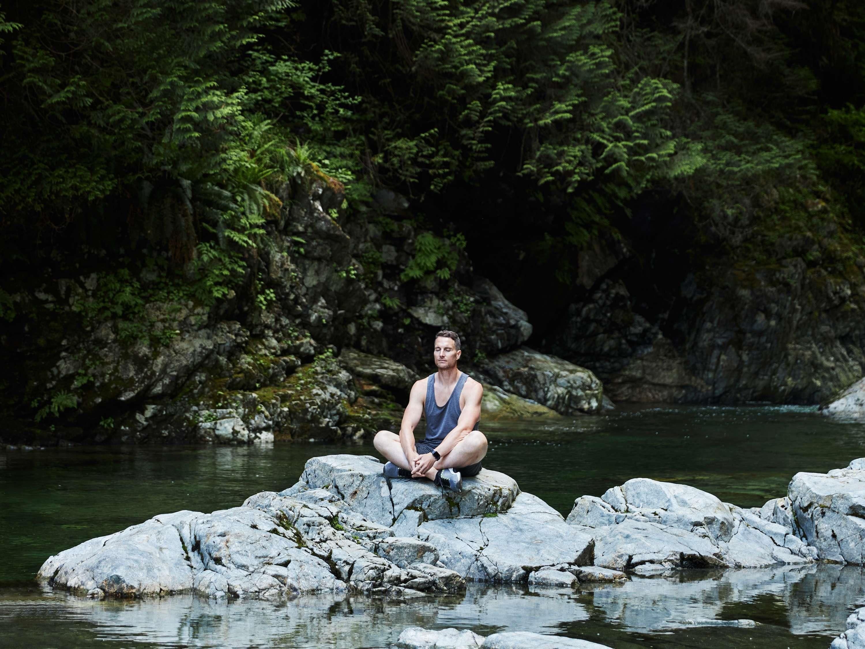 A person sitting on rocks by a river surrounded by dense forest.