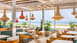 A beachside restaurant with outdoor seating, large windows, and hanging wicker lamps. - Fairmont La Hacienda Costa del Sol (San Roque)