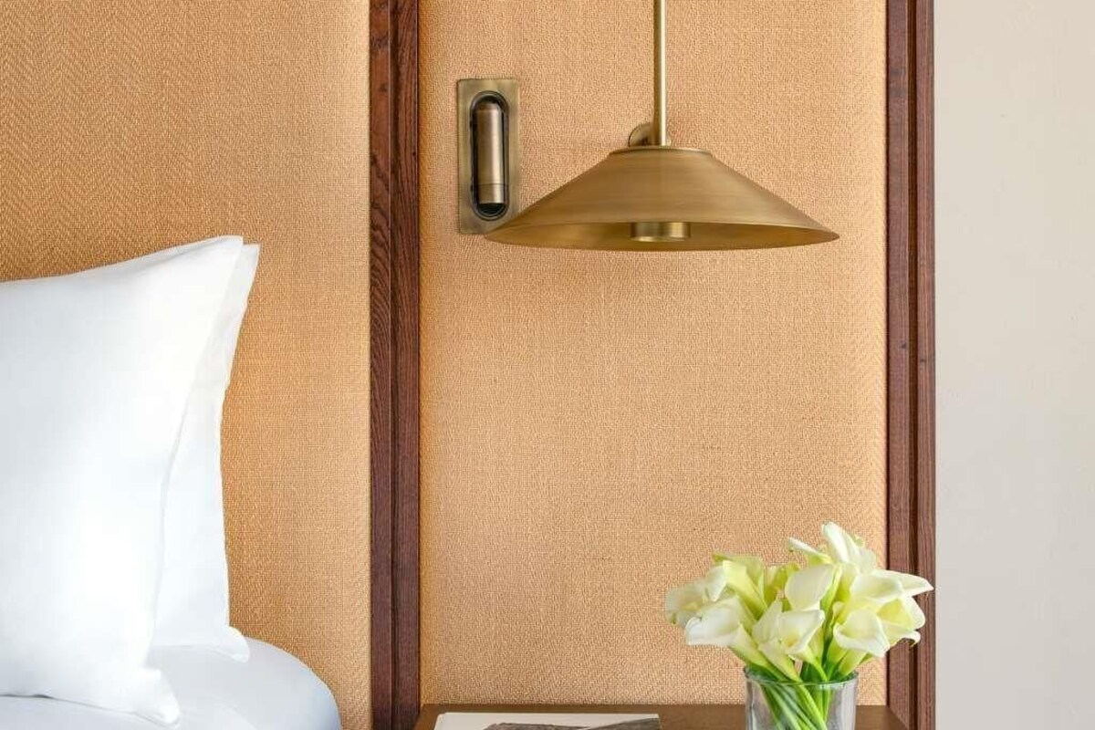 A hotel room with a textured wall, a bedside table with a vase of flowers, and a hanging lamp.