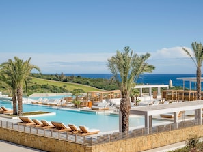 A pool area with lounge chairs and palm trees, overlooking a golf course and the ocean. - Fairmont La Hacienda Costa del Sol (San Roque)