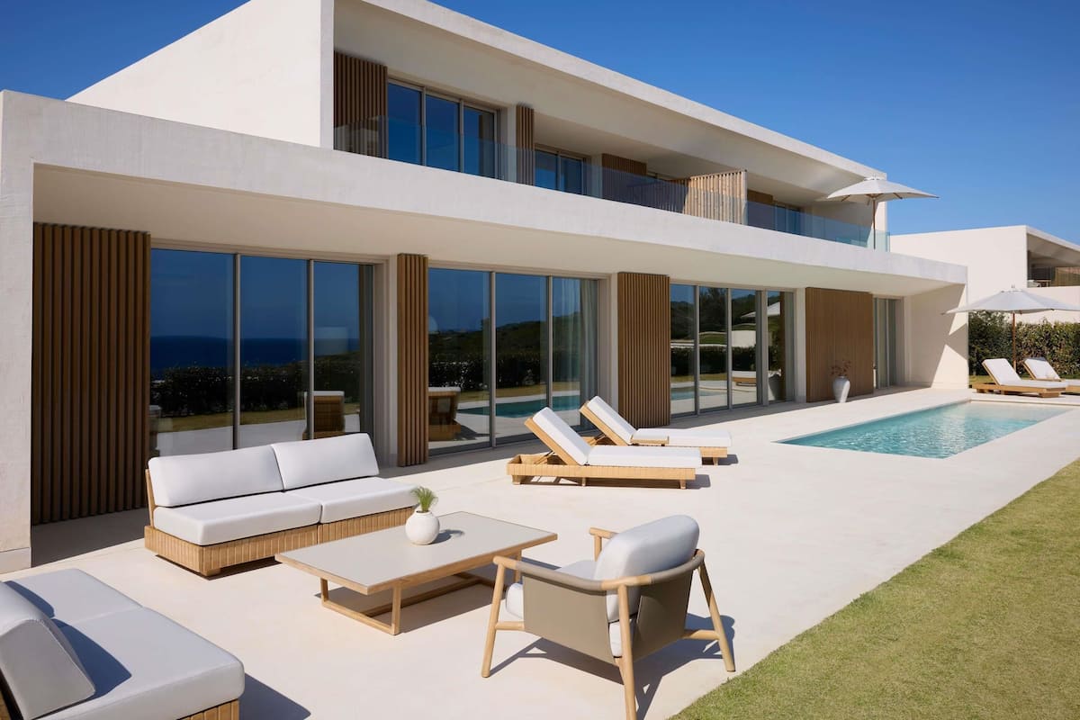 Una casa moderna de dos pisos con piscina, mobiliario exterior y amplias ventanas.