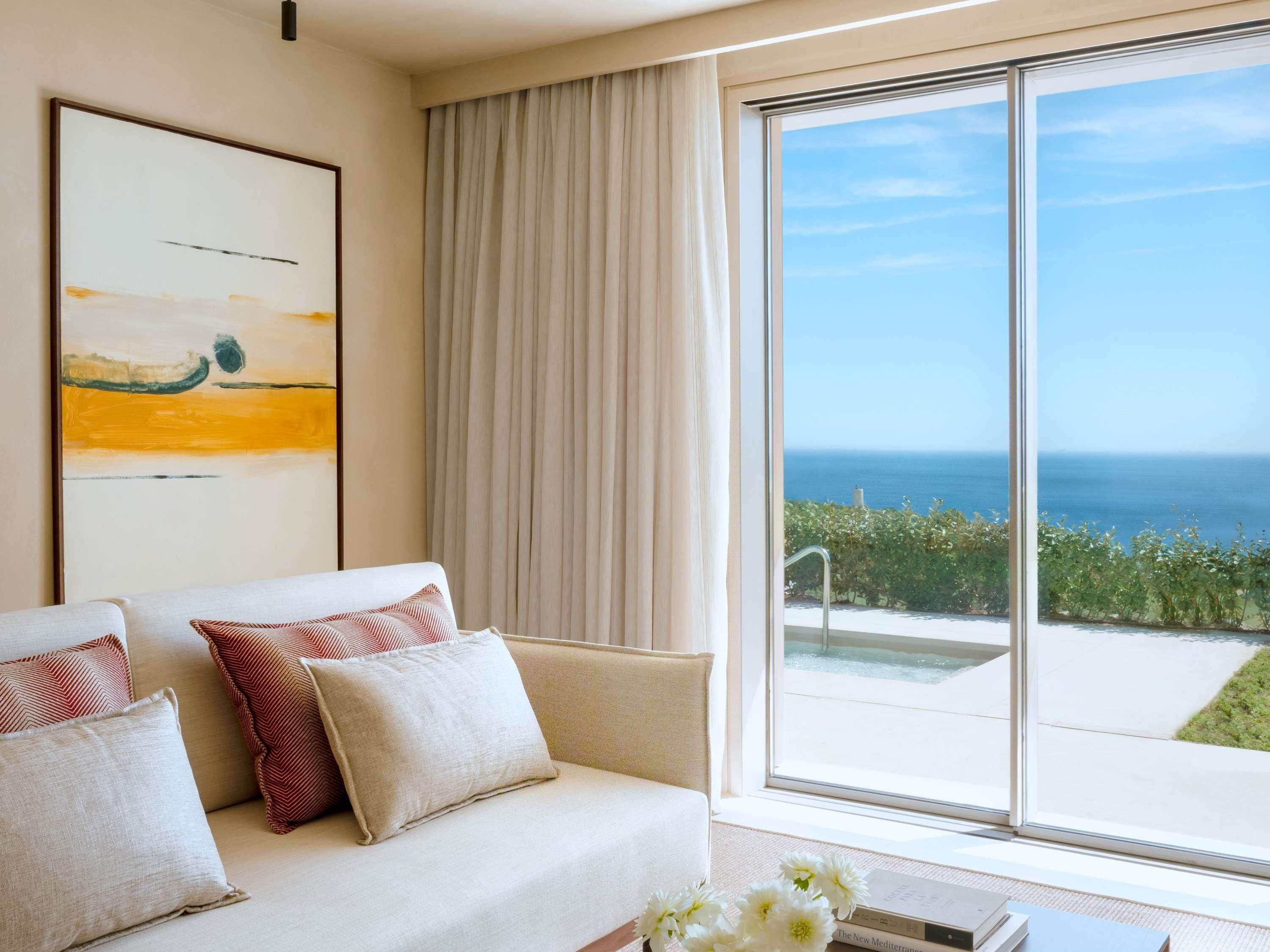 A room with a sofa, a painting, and a view of the sea.