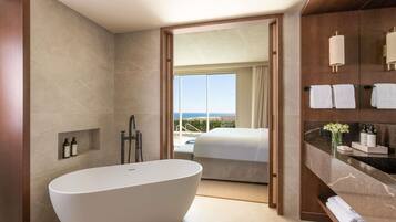 Un baño moderno con una bañera independiente, un tocador con encimera de mármol y vistas a un balcón con cama.