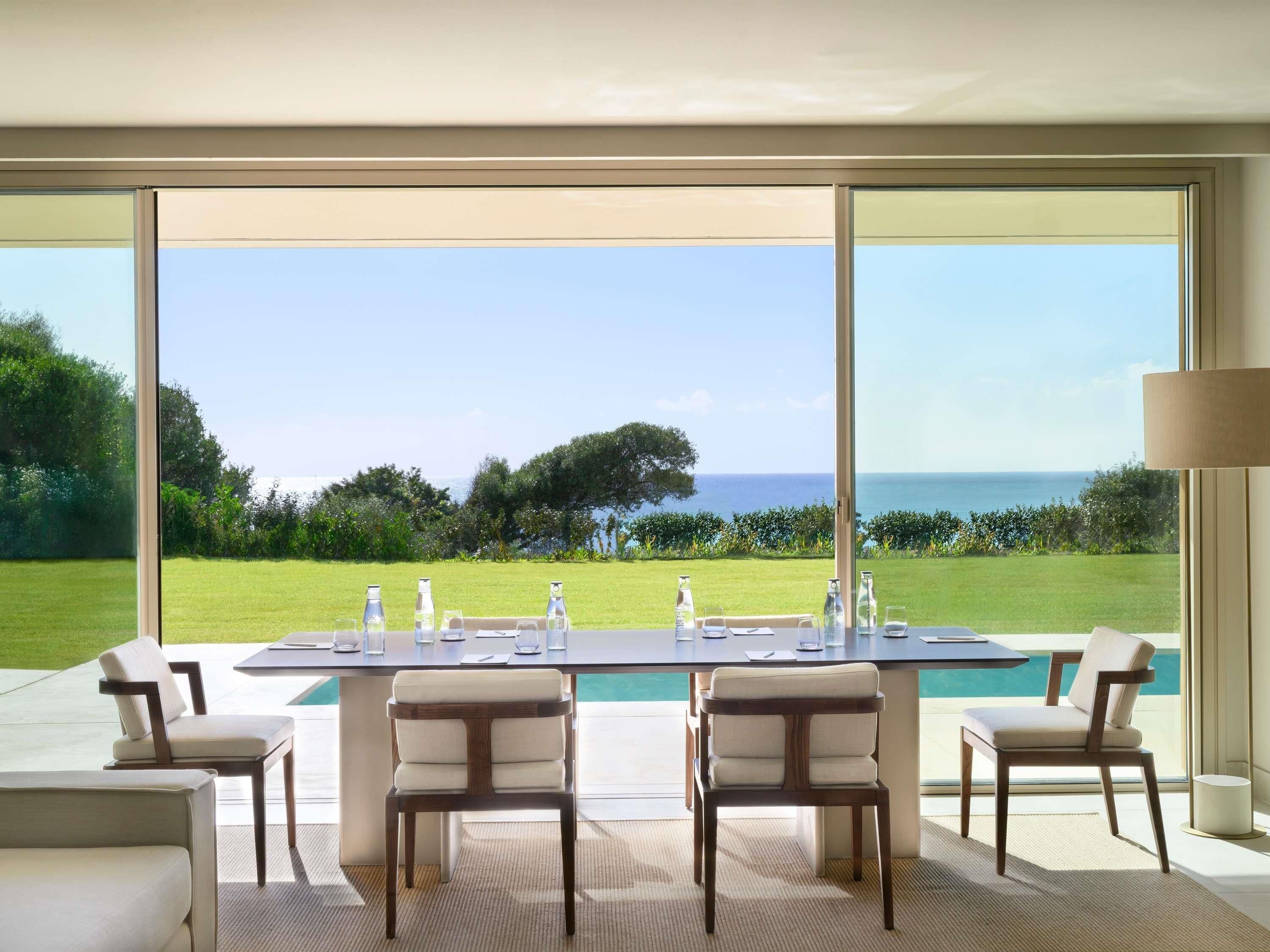 A dining area with a table set for six, overlooking a pool and a view of the sea.